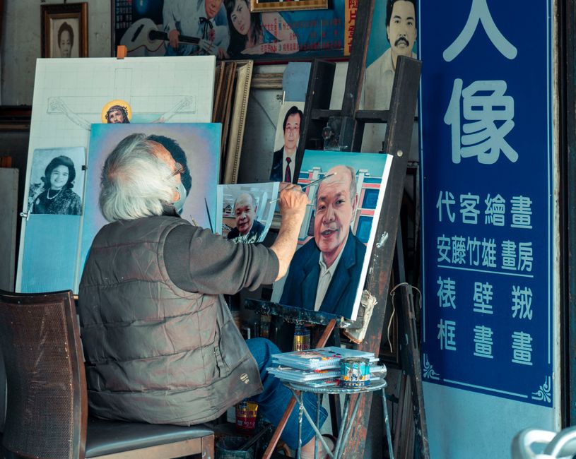 Senior artist captures portraits in a creative studio, surrounded by artwork and tools of his trade.