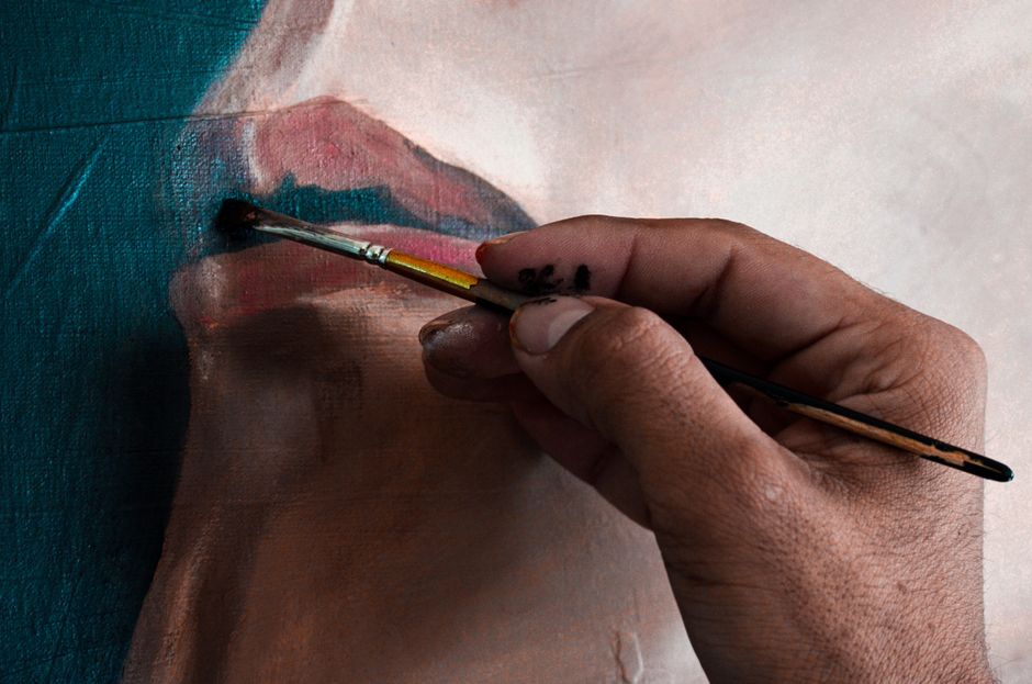 A detailed view of a hand using a paintbrush to create a portrait on canvas, showcasing artistic creativity.